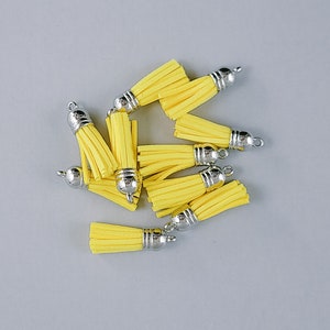 May include: A group of eight yellow fabric tassels with silver metal caps. The tassels are arranged in a pile on a gray surface.