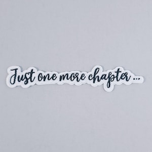 Op de afbeelding: Een witte patch met de tekst "Just one more chapter..." in donkerblauwe cursieve letters. De patch heeft een witte rand en staat op een lichtgrijze achtergrond. Het ontwerp is eenvoudig en tekstgericht.