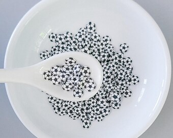 Può includere: Una ciotola bianca piena di coriandoli a forma di pallone da calcio bianco e nero. I coriandoli vengono raccolti con un cucchiaio bianco.