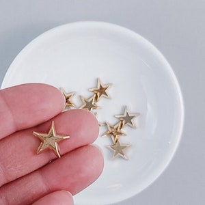 May include: A small bowl filled with gold star-shaped embellishments. One star is being held by a hand.