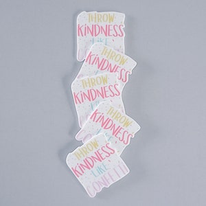 May include: A stack of white square cards with pink and gold lettering that reads "Throw Kindness Like Confetti".