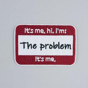 Könnte beinhalten: Ein rotes und weißes Namensschild mit dem Text "It's me, hi I'm: The problem. It's me."