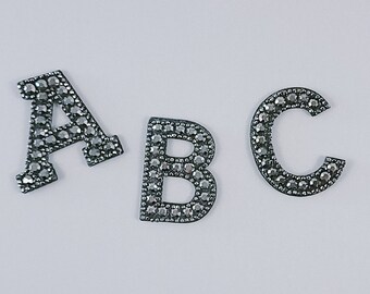 Peut inclure: Trois lettres argentées, A, B et C, sont faites de strass. Les lettres sont sur un fond blanc.