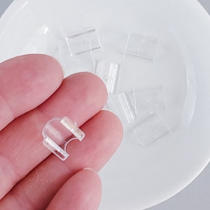 Op de afbeelding: Een close-up van een transparante plastic gordijnclip. De clip is ontworpen om een gordijnroede op zijn plaats te houden.