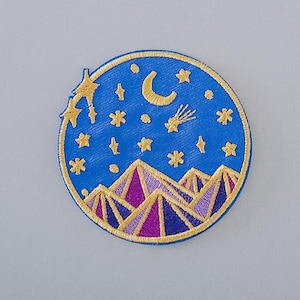 May include: A blue embroidered patch with a crescent moon, stars, and a shooting star above a purple and gold mountain range.