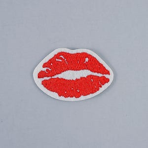 Könnte beinhalten: Gestickter Aufnäher mit einem Paar roter Lippen mit weißem Rand. Die Lippen sind leuchtend rot und mit einem strukturierten Faden genäht. Der Aufnäher ist zum Aufbügeln oder Aufnähen auf Stoff gedacht.