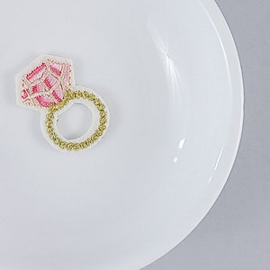 Puede incluir: Un anillo bordado de color rosa y blanco con una banda dorada en un plato blanco.