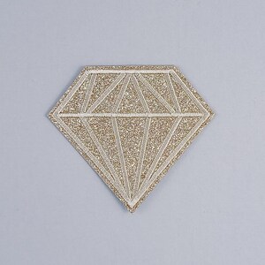 Peut inclure: Un patch en forme de diamant avec des paillettes dorées et un contour blanc.