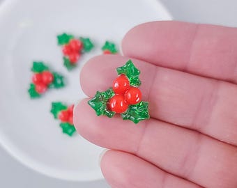 Könnte beinhalten: Nahaufnahme einer roten und grünen Stechpalmenbeere. Die Verzierung ist aus Kunststoff und hat eine glänzende Oberfläche. Es ist eine beliebte Dekoration für Weihnachtsbastelarbeiten.