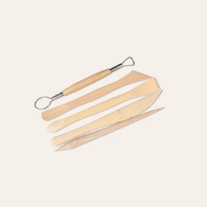 May include: A set of five light wood clay sculpting tools. The tools include a loop tool, a serrated edge tool, a knife-shaped tool, a pointed tool, and a flat tool. The tools are arranged on a light background.