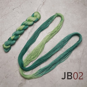 Op de afbeelding: Twee bollen groene borduurgaren, &eacute;&eacute;n bol is gedraaid en de andere ligt plat. De bollen liggen op een grijs marmeren oppervlak. De tekst "JB02" is op het oppervlak gedrukt.