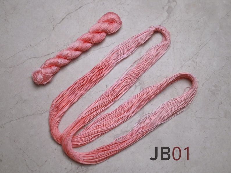 Op de afbeelding: Een bolletje lichtroze borduurgaren, met een lange streng van hetzelfde garen ernaast gelegd. De tekst "JB01" is gedrukt op een witte achtergrond onder het garen.