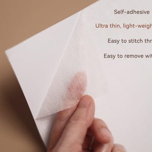 May include: A close-up of a white, self-adhesive material being peeled back, revealing a fingertip. Text on the image reads: Self-adhesive, Ultra thin, light-weight & soft, Easy to stitch through, Easy to remove with water.