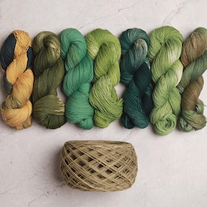 May include: Eight skeins of yarn in shades of green and yellow, arranged in a row. The yarn is wound into balls and is ready for knitting or crocheting. A small basket of yarn is in the foreground.