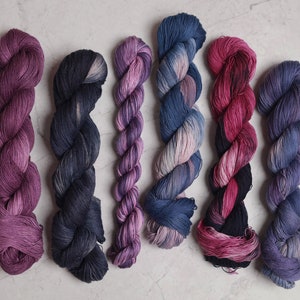 Peut inclure: Sept pelotes de laine dans différentes nuances de violet, rose et bleu. La laine est torsadée et disposée en rangée.