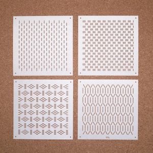 Puede incluir: Cuatro paneles cuadrados blancos con diferentes patrones geométricos recortados. Los paneles están dispuestos en una cuadrícula de 2x2 sobre un fondo de corcho marrón.