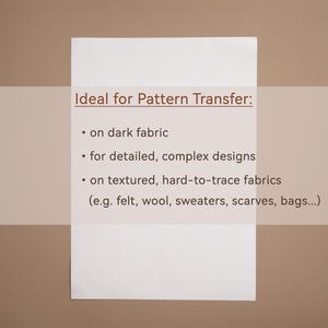 May include: A white rectangular paper with the text "Ideal for Pattern Transfer:" and bullet points listing uses for dark fabric, detailed designs, and textured fabrics like felt, wool, and scarves. The background is a light brown color.