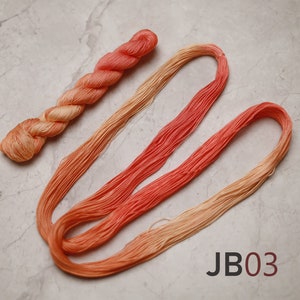 Op de afbeelding: Twee bollen ombre borduurgaren, &eacute;&eacute;n bol is perzik tot oranje, de andere is oranje tot rood. De bollen liggen op een lichtgrijs marmeren oppervlak. De tekst "JB03" is in zwart op het oppervlak gedrukt.