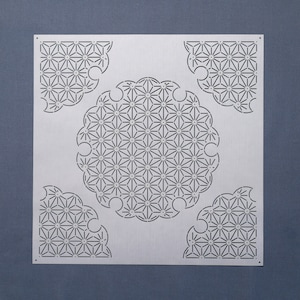 May include: A white metal stencil with a geometric design. The design features a circle in the centre with four corner designs. The circle and corner designs are made up of repeating star shapes.