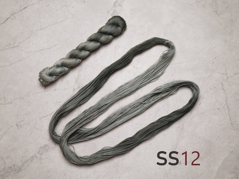 Op de afbeelding: Twee klosjes borduurgaren in een verloop van groene en grijze tinten. De klosjes zijn gerangschikt in een losse lus en een spiraal. De tekst "SS12" is zichtbaar in de rechterbenedenhoek van de afbeelding.