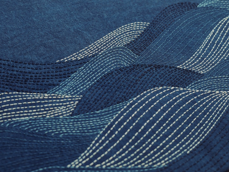 May include: A close-up of a blue fabric with white stitching in a wave pattern.