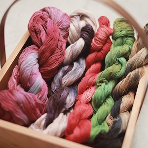 May include: A wooden tray filled with colorful yarn skeins in shades of pink, red, green, brown, and black. The yarn is arranged in a decorative pattern.