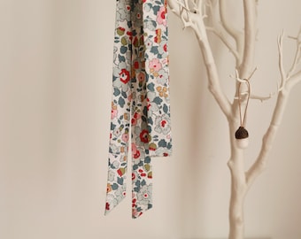 Op de afbeelding: Drie stoffen linten met een bloemenpatroon hangen aan een witte tak. De linten zijn in de kleuren blauw, wit, roze en rood.