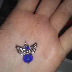 May include: A silver-toned angel pendant with a faceted, deep blue crystal body and detailed wings. The pendant is small and delicate, designed to be worn as jewelry.