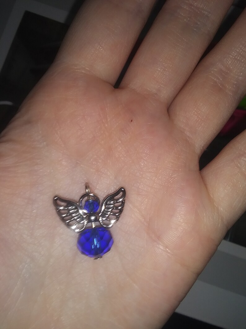 May include: A silver-toned angel pendant with a faceted, deep blue crystal body and detailed wings. The pendant is small and delicate, designed to be worn as jewelry.