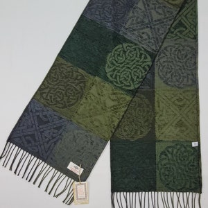 Può includere: Una sciarpa verde e grigia con un motivo a nodo celtico. La sciarpa ha frange su entrambe le estremità e un'etichetta che dice "Galway".