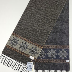 Peut inclure: Écharpe grise et marron avec un motif texturé et des franges. La bordure décorative présente des motifs en forme de flocons de neige bleus, beiges et gris. L'étiquette indique "Viking".