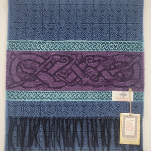 May include: A blue and purple patterned scarf with a black fringe. The scarf has a woven Celtic knot design and a label that reads "Calzeati - Great Collection".