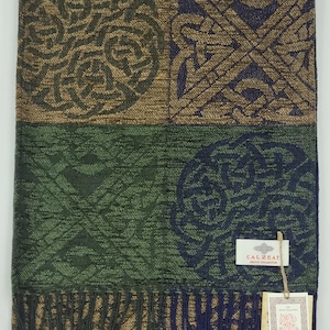 May include: A rectangular scarf with a Celtic knot design in shades of brown, green, and navy blue. The scarf has a fringed edge and a tag that reads "CALZEAT Celtic Collection".