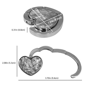 K&ouml;nnte beinhalten: Ein silberfarbener herzf&ouml;rmiger Handtaschenhaken mit Perlmutt-Inlay. Der Haken ist 9,4 cm lang, wenn er ausgeklappt ist, und 5,3 cm hoch. Das Herz ist 4,7 cm x 4,2 cm gro&szlig;.