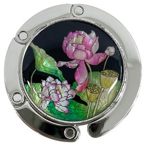 May include: A silver-toned purse hook with a black background featuring a pink and white lotus flower design. The hook has a circular shape with a hinged opening and a decorative floral motif.