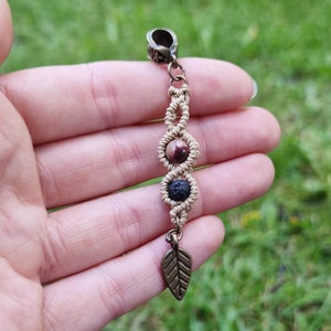 Puede incluir: Un charm de macram&eacute; hecho a mano con un cierre y un dije de hoja de color bronce. El charm presenta tres secciones decorativas con cuentas de piedra natural. Las cuentas son una mezcla de marr&oacute;n y negro, conectadas por nudos de macram&eacute; beige.