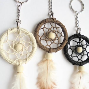 May include: Three dreamcatcher keychains in cream, brown, and black. Each features a woven web design, a wooden bead, and a feather. The keychains have silver metal rings and chains.