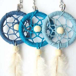 May include: Three handmade dreamcatcher keychains in shades of blue. Each features a woven web design, a wooden bead, and a feather. The keychains are attached to silver-colored metal rings.
