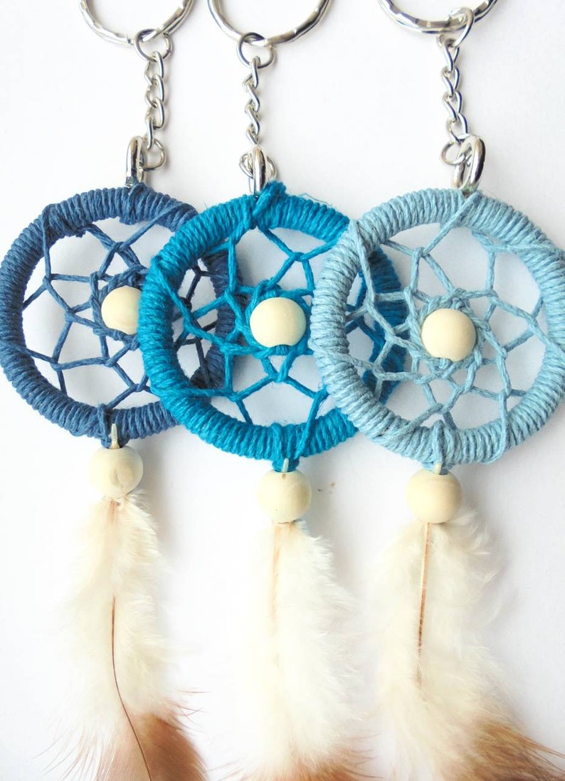 May include: Three handmade dreamcatcher keychains in shades of blue. Each features a woven web design, a wooden bead, and a feather. The keychains are attached to silver-colored metal rings.