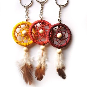 May include: Three dreamcatcher keychains in yellow, orange, and red. Each keychain features a woven web design, a wooden bead, and hanging feathers. The keychains have silver metal rings and chains.