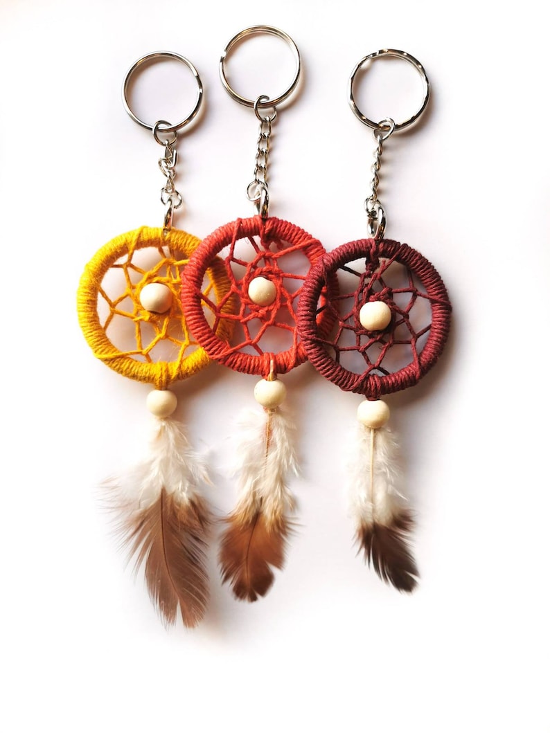 May include: Three dreamcatcher keychains in yellow, orange, and red. Each keychain features a woven web design, a wooden bead, and hanging feathers. The keychains have silver metal rings and chains.