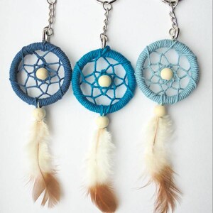 May include: Three dreamcatcher keychains in shades of blue. Each keychain features a woven web within a circular frame, a wooden bead, and a feather. The keychains are attached to silver-colored key rings.