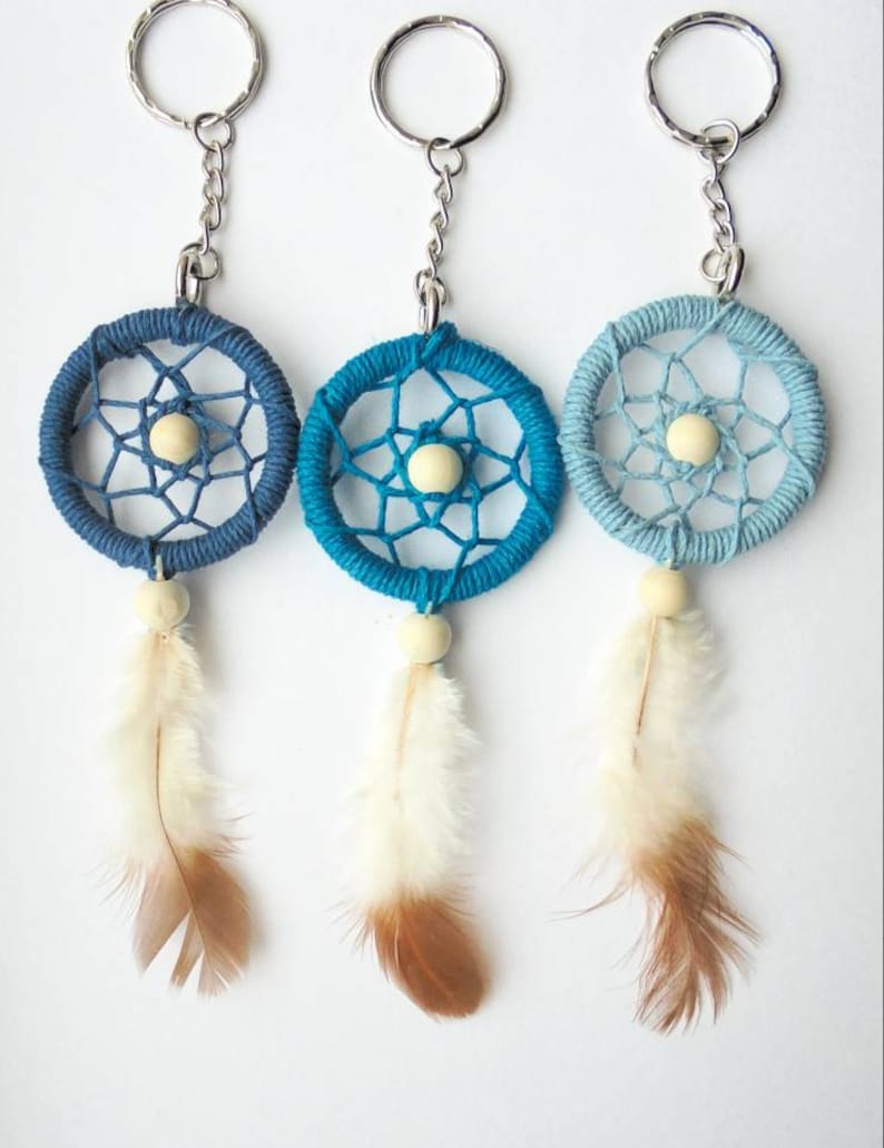 May include: Three dreamcatcher keychains in shades of blue. Each keychain features a woven web within a circular frame, a wooden bead, and a feather. The keychains are attached to silver-colored key rings.