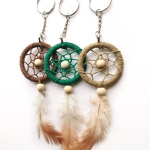 May include: Three dreamcatcher keychains in brown, green, and tan. Each features a woven web design, a wooden bead, and hanging feathers. The keychains have silver-colored metal rings and chains.
