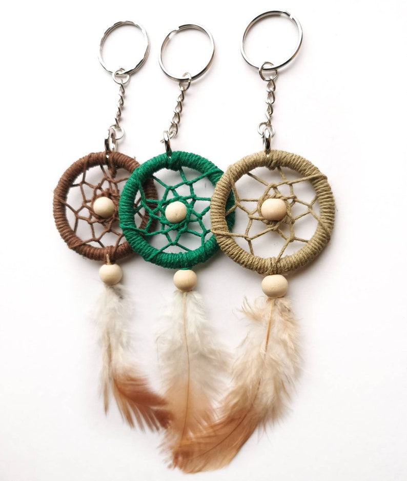 May include: Three dreamcatcher keychains in brown, green, and tan. Each features a woven web design, a wooden bead, and hanging feathers. The keychains have silver-colored metal rings and chains.