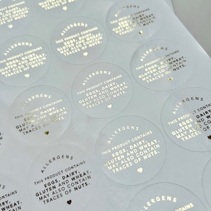 May include: Circular transparent stickers with gold lettering. Each sticker reads "ALLERGENS" and lists potential allergens: eggs, dairy, gluten, wheat, and traces of nuts. A small heart is printed below the text.