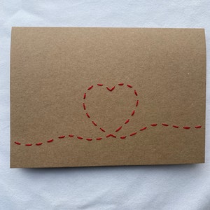 May include: A brown card with a red stitched heart and a red stitched line across the bottom.
