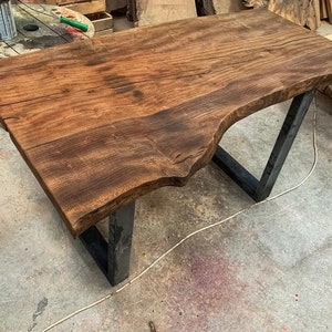 May include: A large, dark brown wooden table top with a live edge, supported by black metal legs. The table top has a natural, rustic finish.