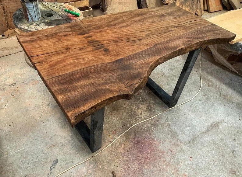 May include: A large, dark brown wooden table top with a live edge, supported by black metal legs. The table top has a natural, rustic finish.