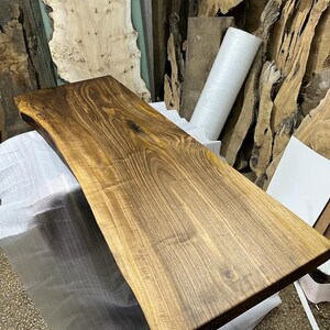 May include: A large, natural wood slab with a live edge. The wood is a rich brown color with a natural grain pattern. The slab is smooth and polished, and it would be perfect for a table top or countertop.